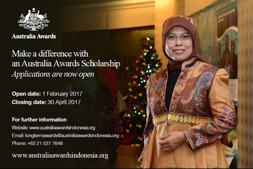 A woman with glasses and brown hijab wearing orange batik dress standing